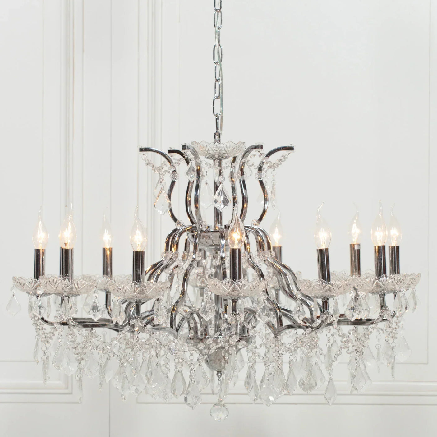 Crystal chandelier with chrome frame and candle-style lights hanging in white room