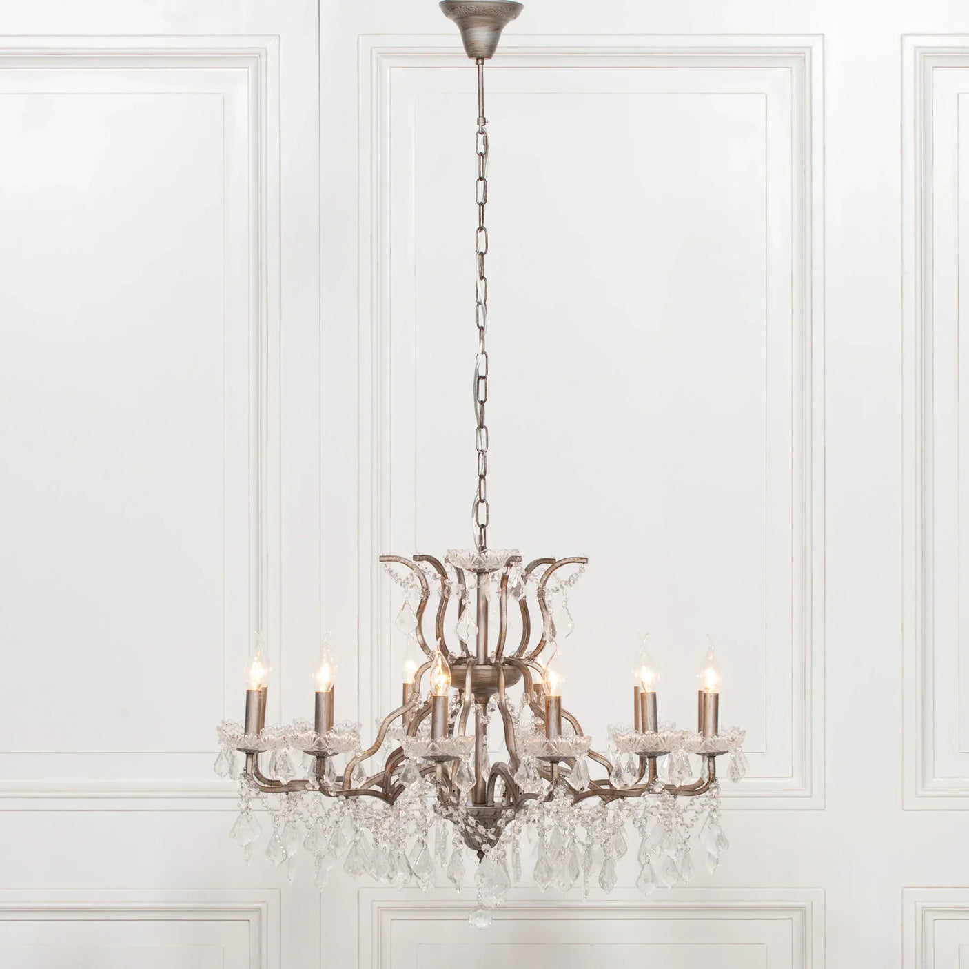 Crystal chandelier with six candle bulbs and hanging glass droplets against white panelled wall