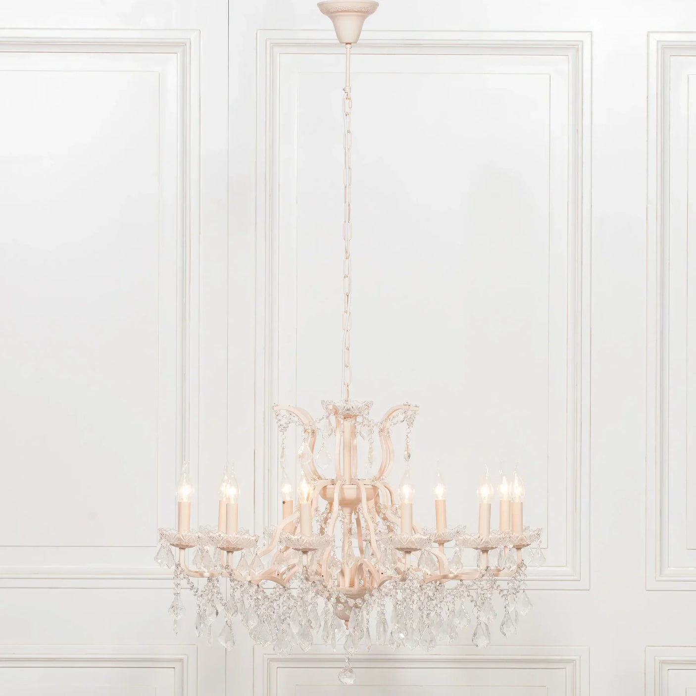 Crystal chandelier with candle-style lights and hanging glass droplets against white panel wall