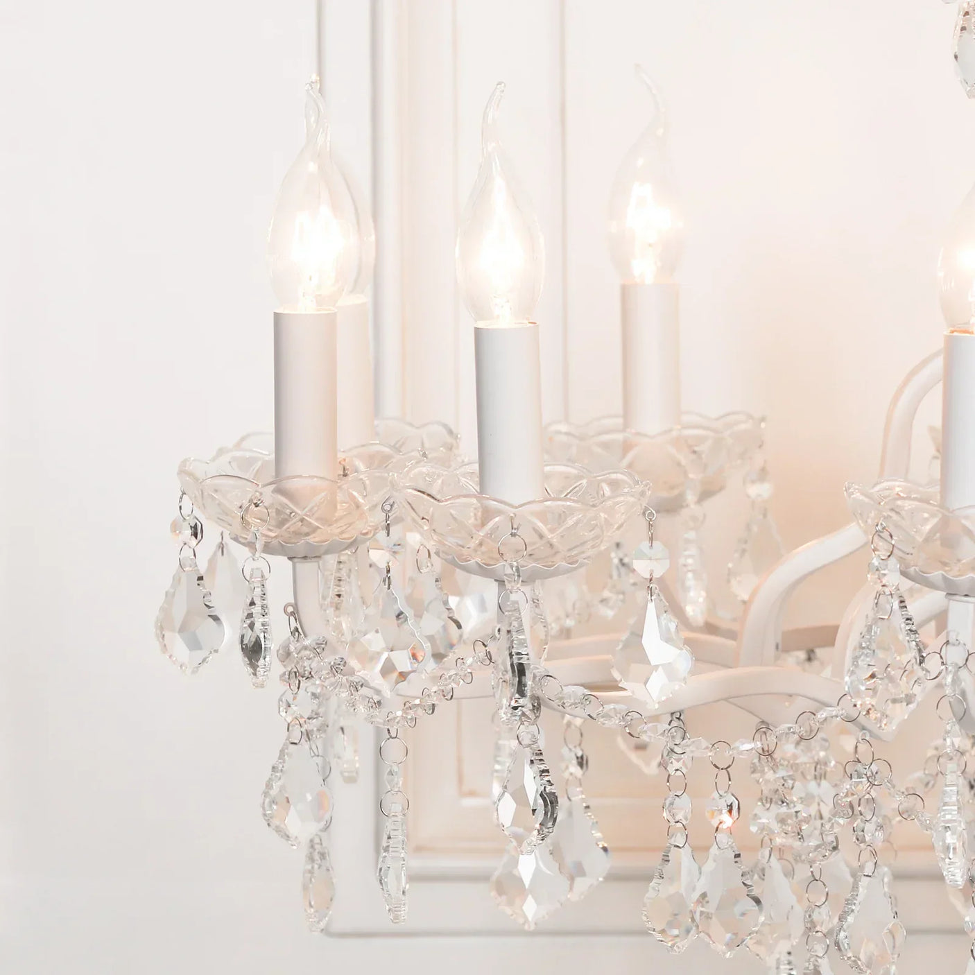 Closeup of white crystal chandelier with teardrop pendants and candle-style bulbs