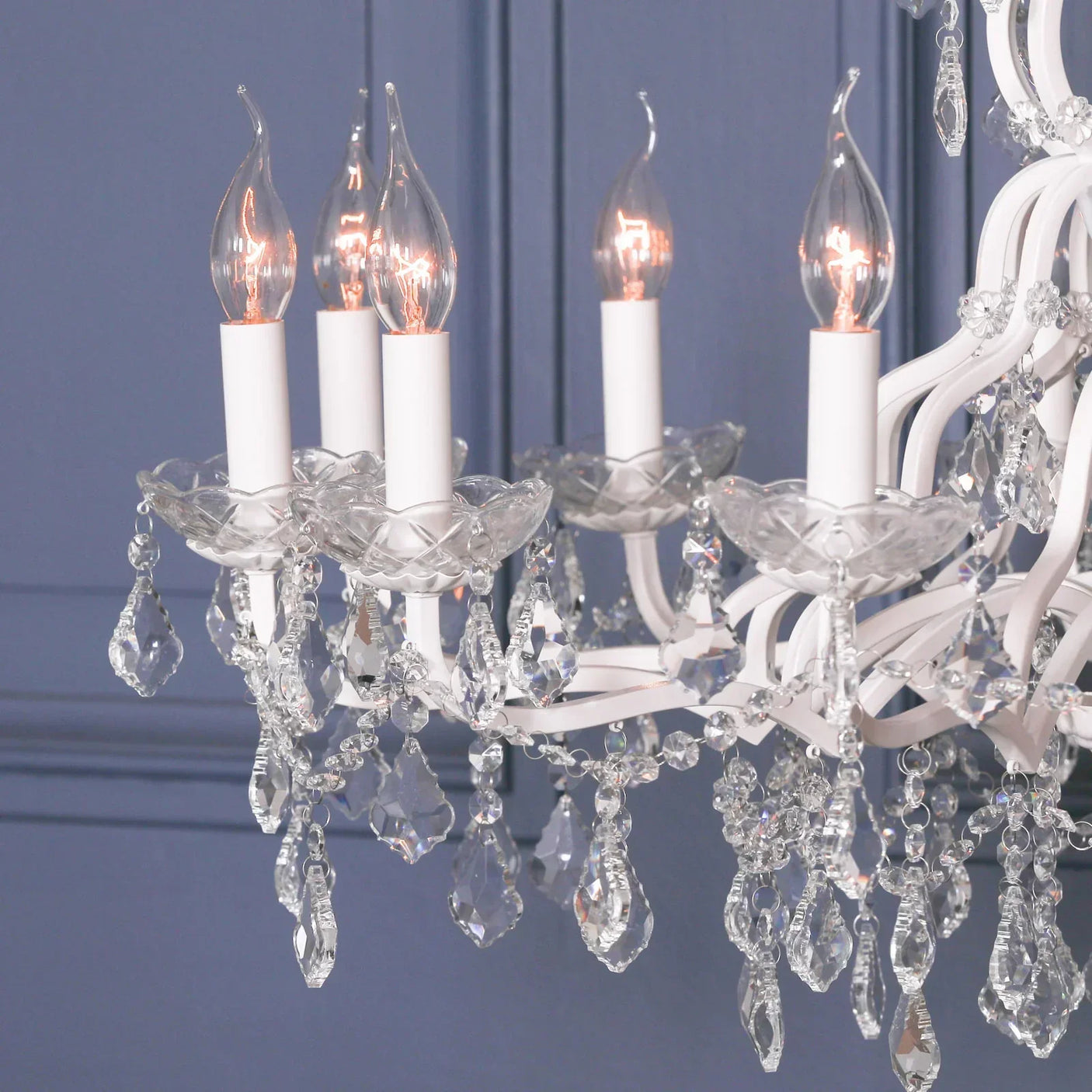 Crystal chandelier with five candle lights and glass droplets against blue paneled wall