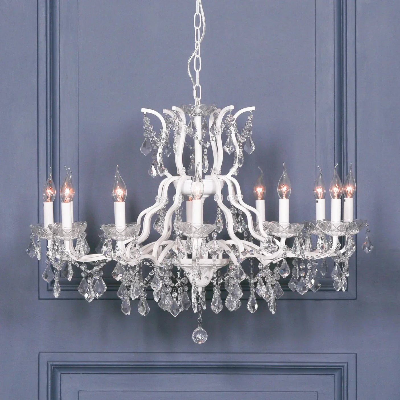 White crystal chandelier with twelve candle lights and hanging droplets against blue wall