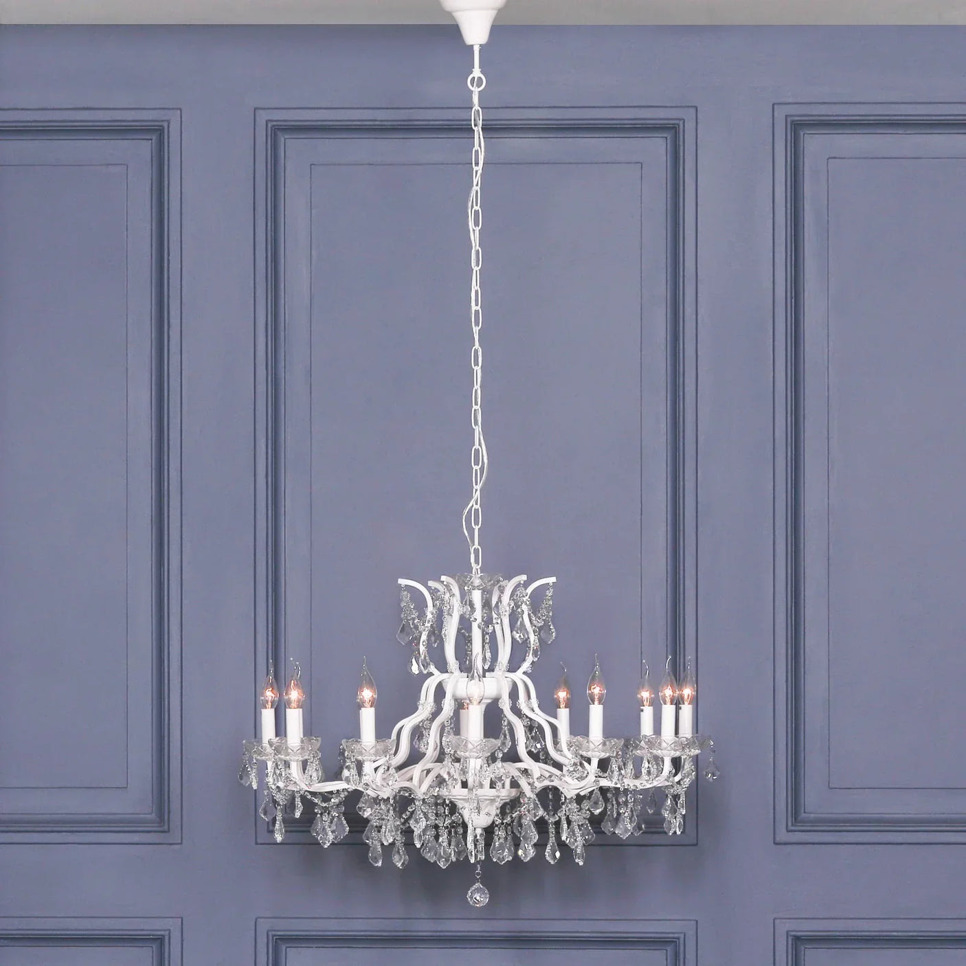 White crystal chandelier with candle-style bulbs hanging against a panelled grey wall
