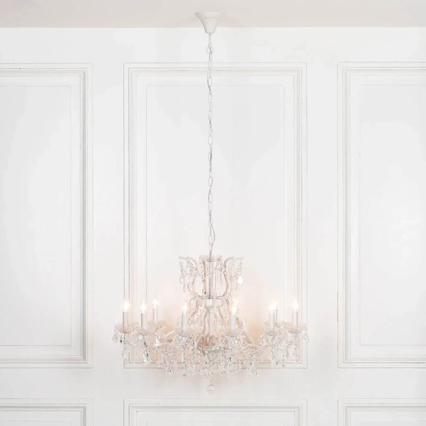 Crystal chandelier with candle-style lights hanging in a white paneled room