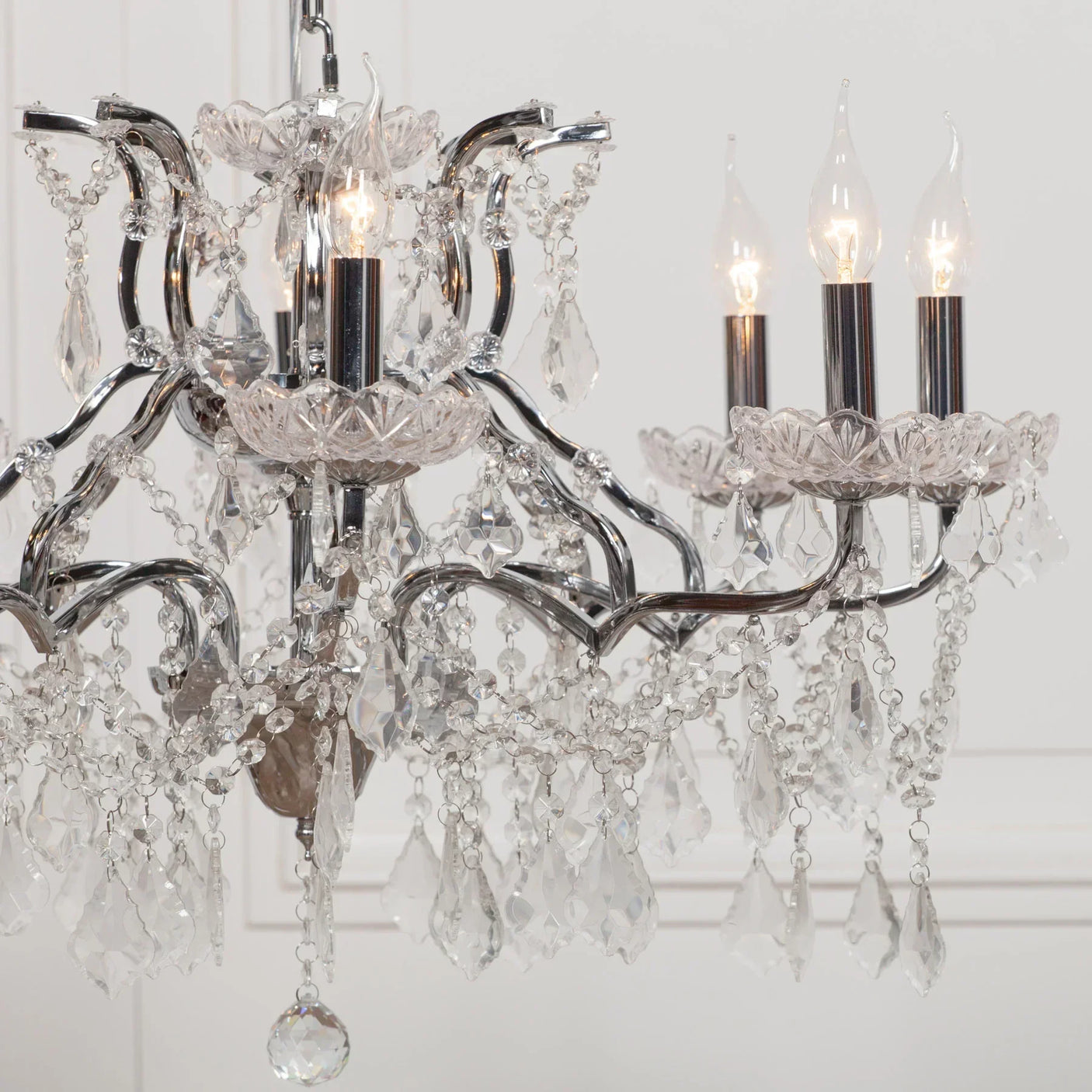 Crystal chandelier with chrome arms and hanging glass droplets in a white interior