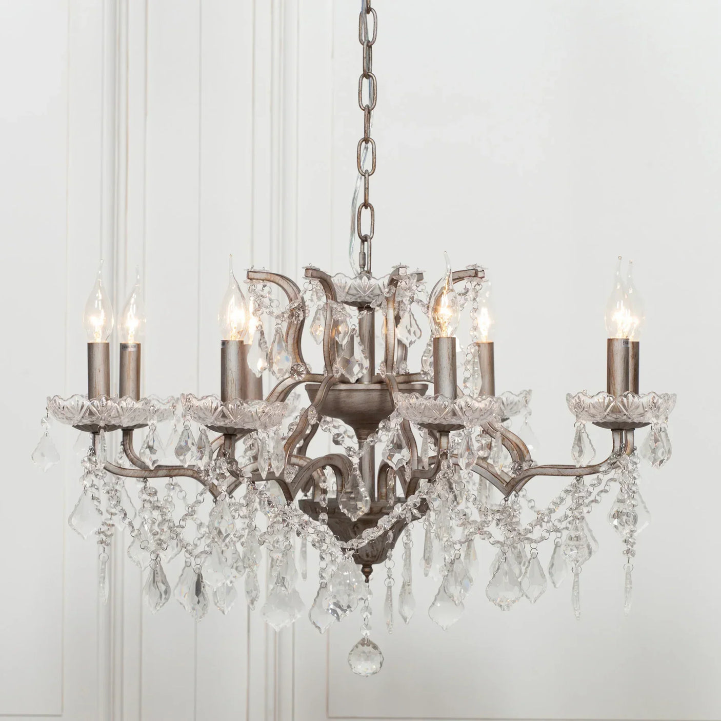 Crystal chandelier with six candle-style lights and metal frame against white wall