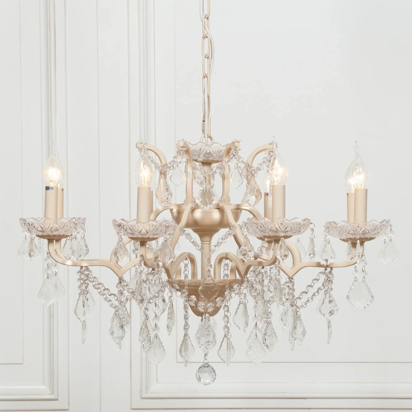 Cream chandelier with glass drops and candle-style lights against white panel wall