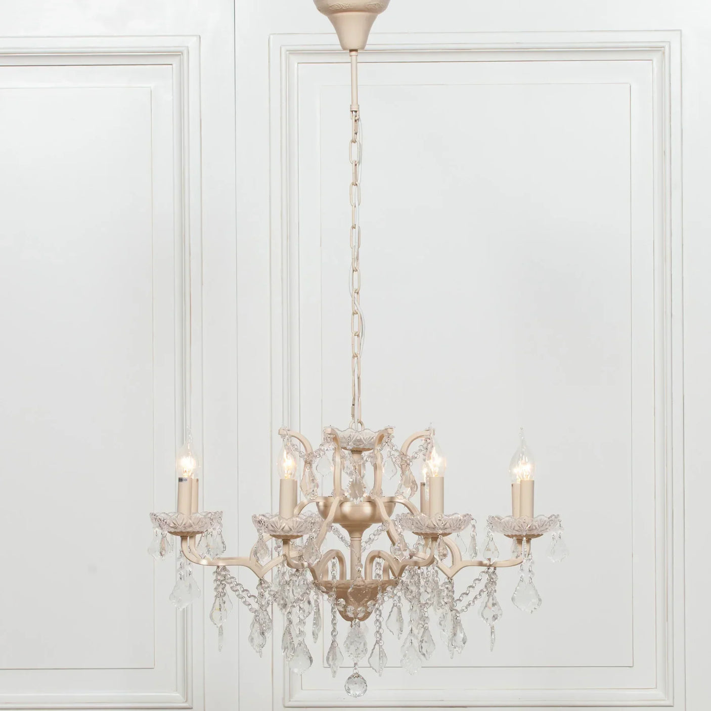 Gold chandelier with crystal accents and candle-style lights against white panelled wall
