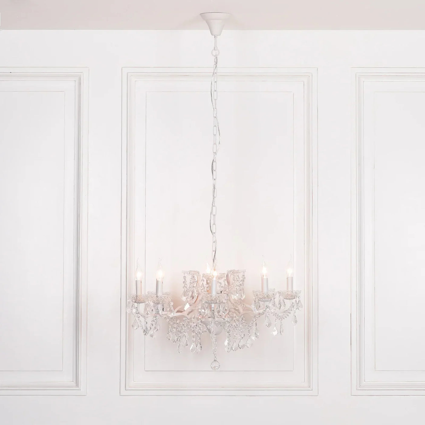 Crystal chandelier with candle-style lights hanging in white paneled room