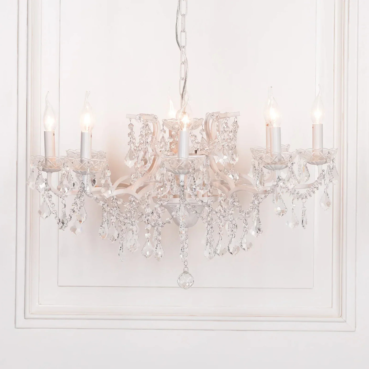 Crystal chandelier with six candle-style lights and hanging glass drops against white wall