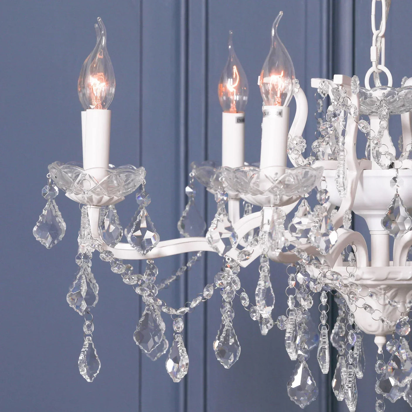 White crystal chandelier with candle-style bulbs and teardrop hanging crystals against blue wall