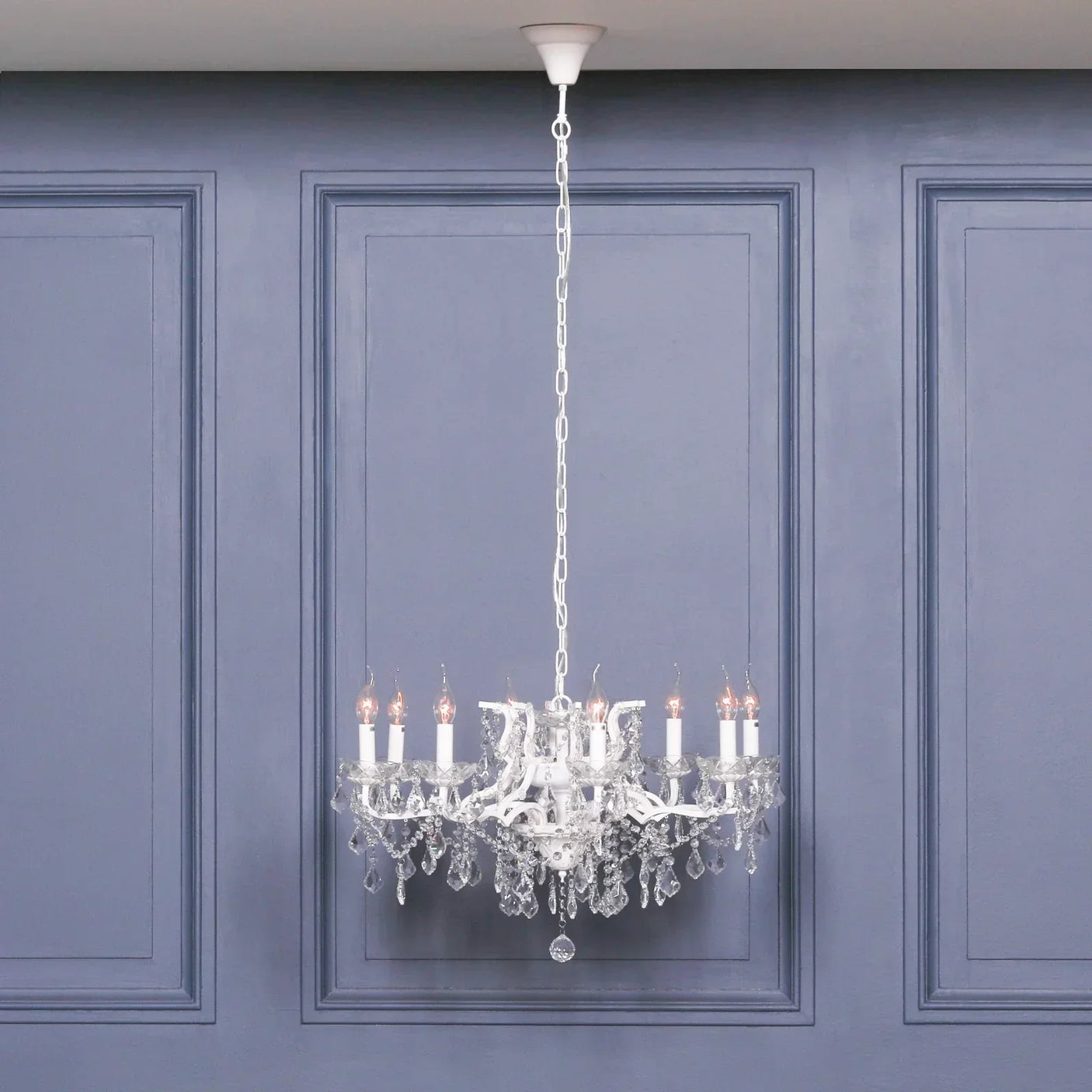 Crystal chandelier with candle-style bulbs and hanging glass droplets against blue panel wall