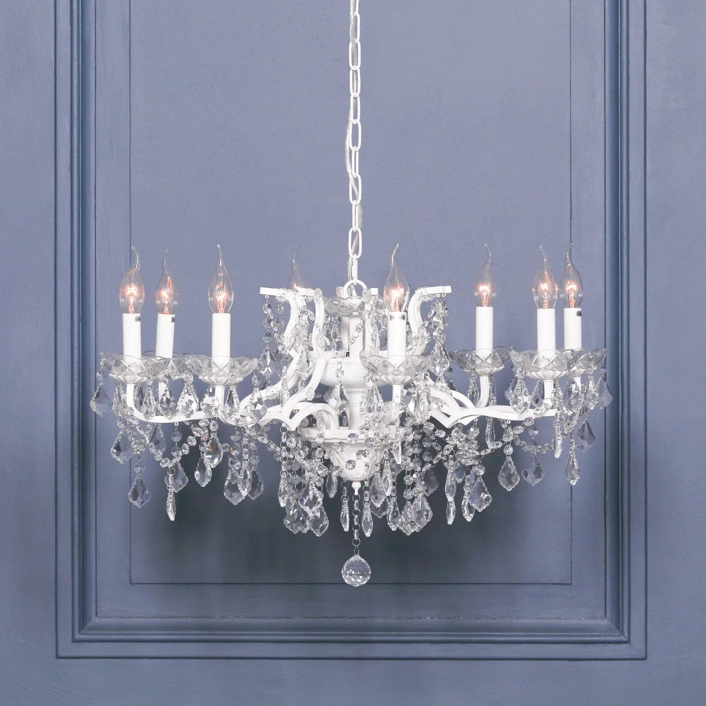 White crystal chandelier with eight candle-style lights against blue panelled wall