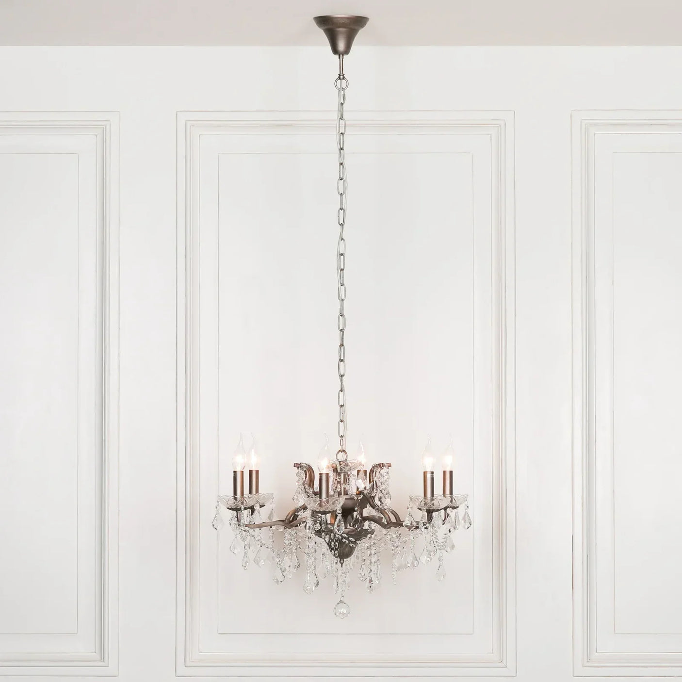 Crystal chandelier with chrome finish and candle-style bulbs hanging in white paneled room
