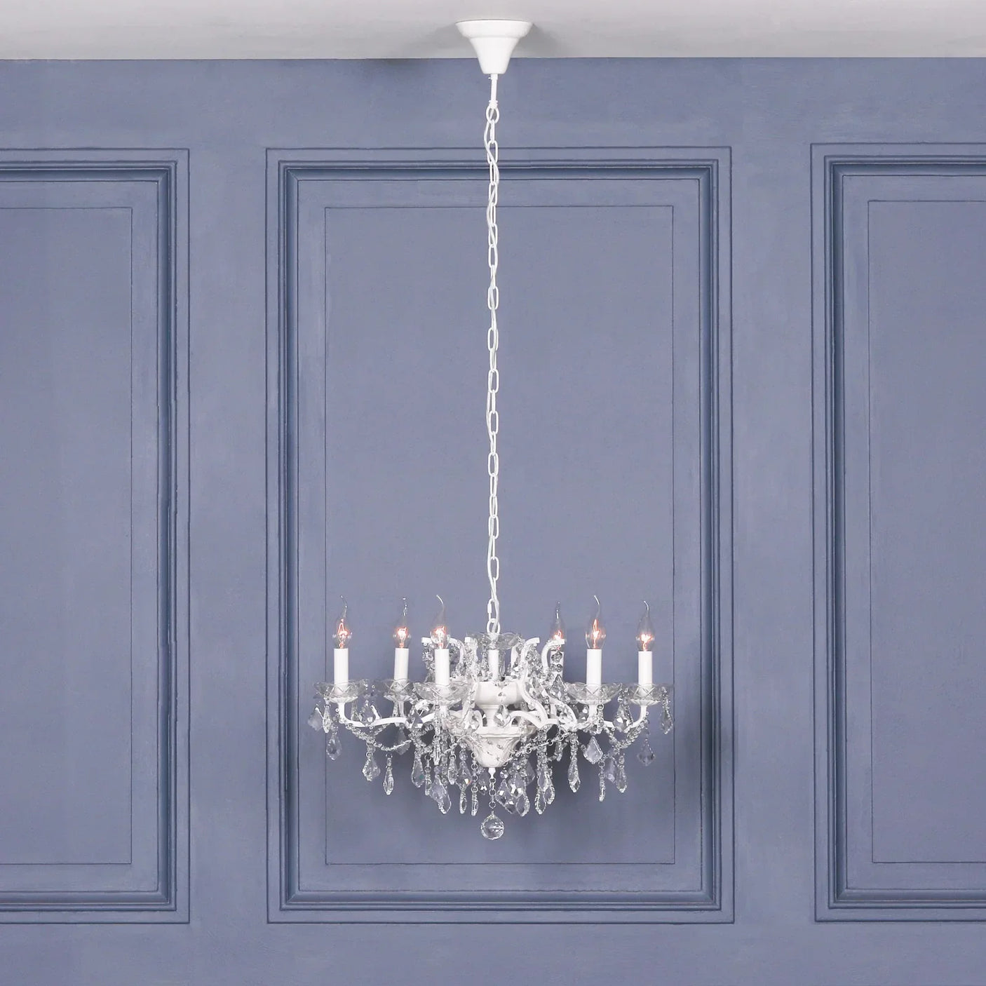 Crystal chandelier lighting with candle bulbs hanging from ceiling against blue panelled wall