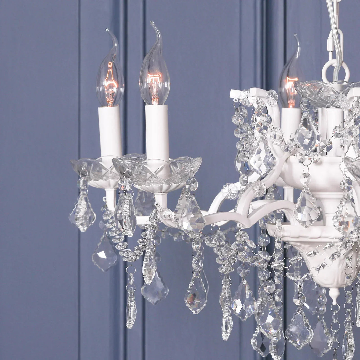 Glass crystal chandelier with white candle-style lights against blue panel wall