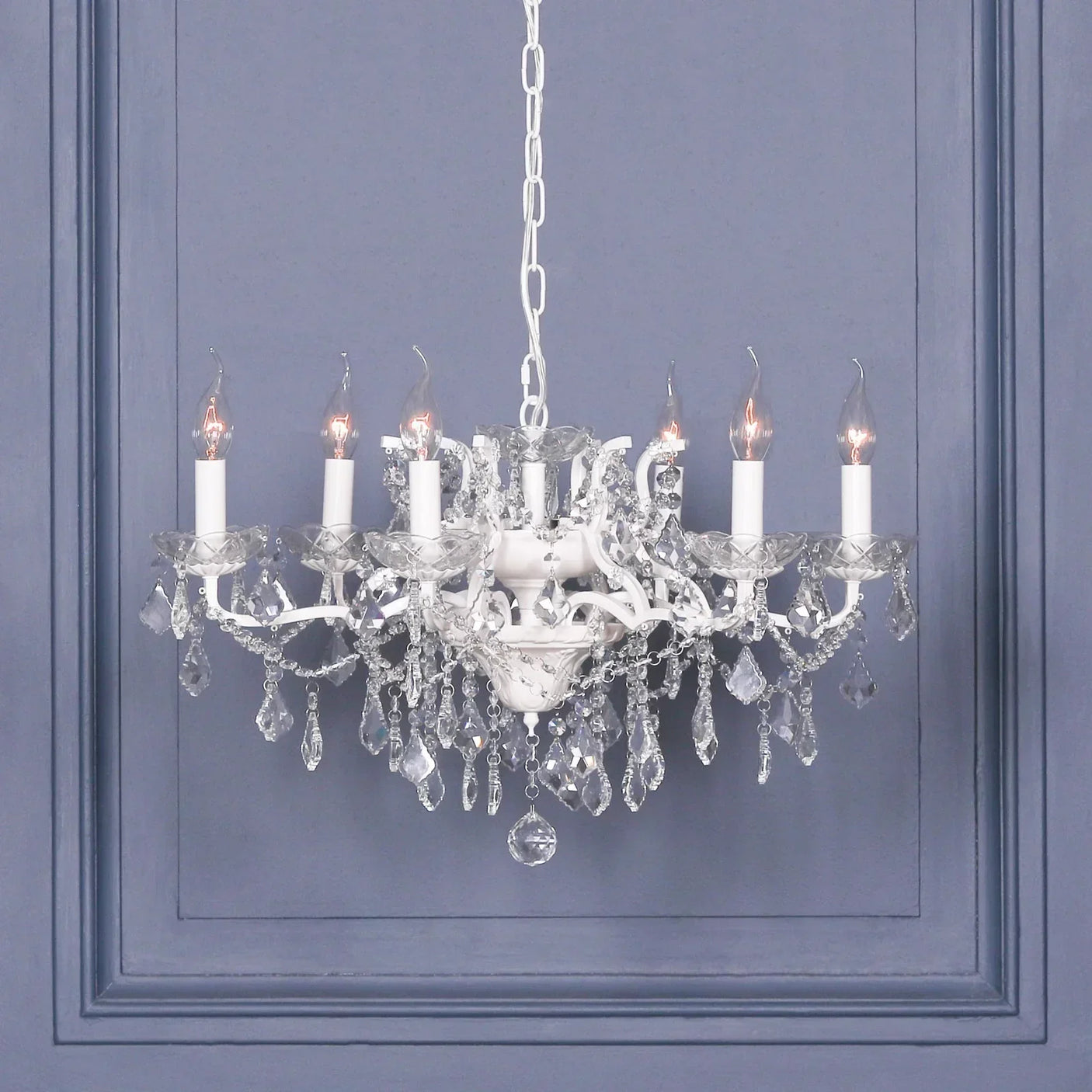 Crystal chandelier with six candle-style lights and hanging glass pendants against blue wall