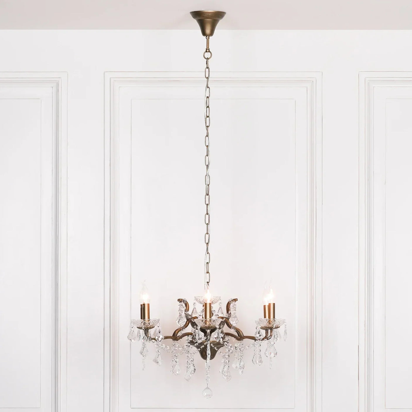 Brass and crystal chandelier with four candle bulbs hanging against white paneled wall