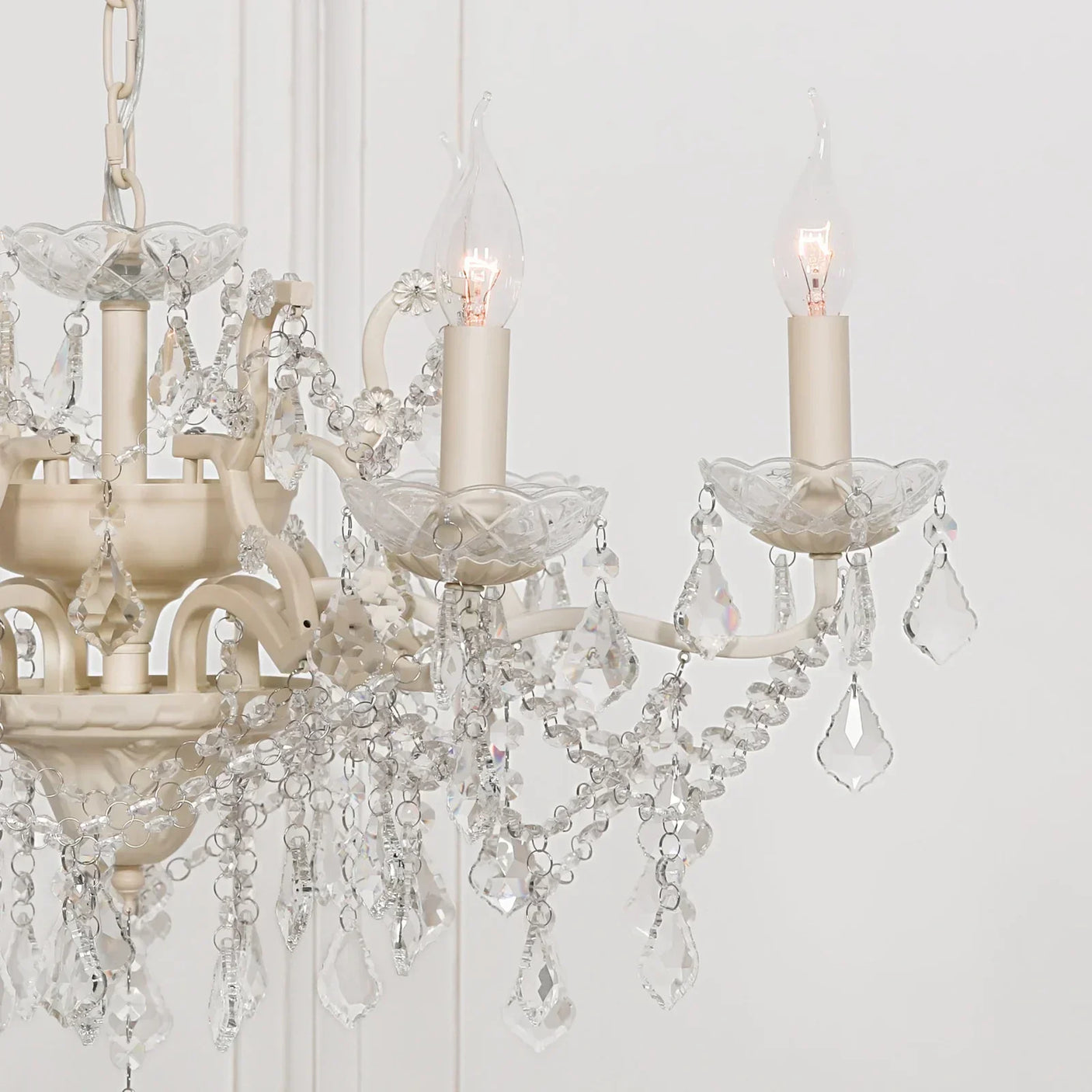 Cream crystal chandelier with candle-effect bulbs and hanging glass droplets close up