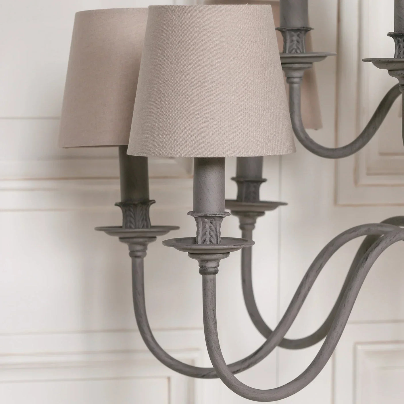 grey metal chandelier with beige fabric lampshades close-up against white panel wall
