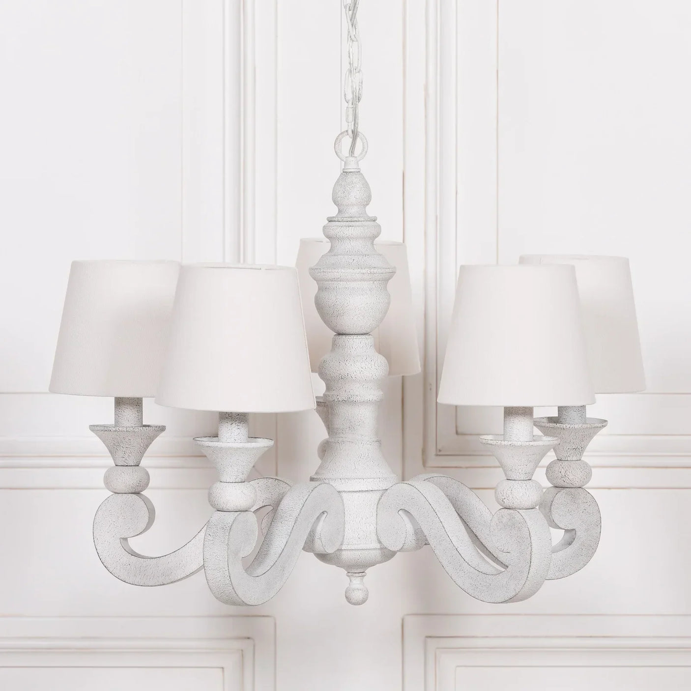 White wooden chandelier with six fabric lampshades, hanging in front of panelled wall