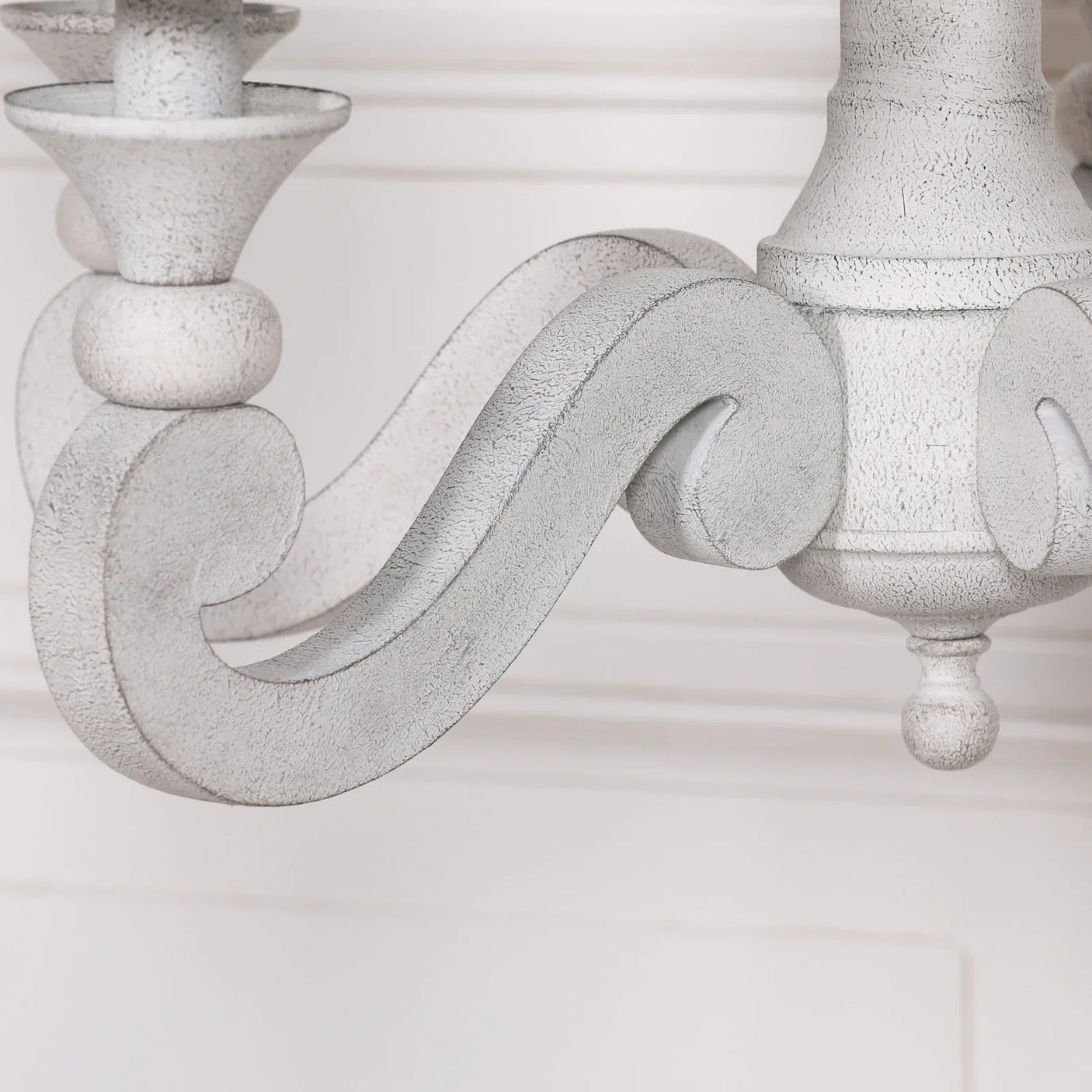Close-up of distressed white wood chandelier arm with ornate scroll detail