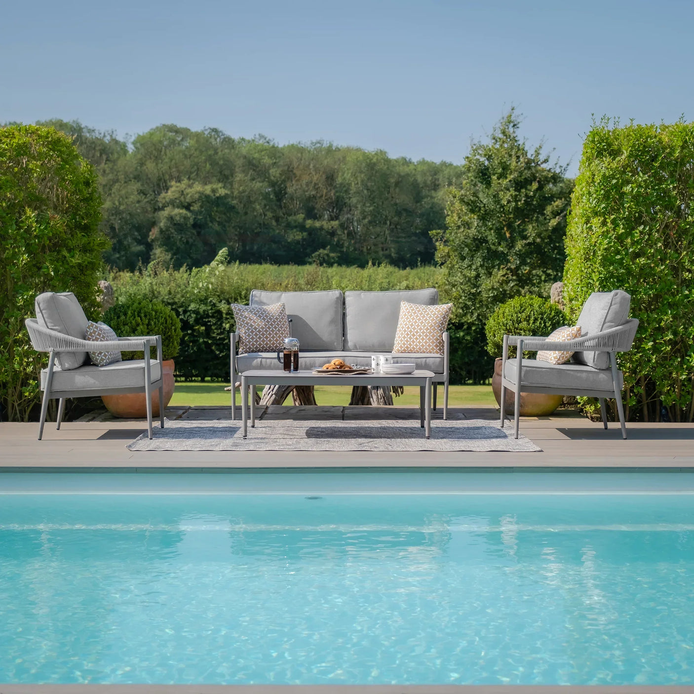 Grey outdoor garden furniture set with sofa, armchairs and table beside swimming pool