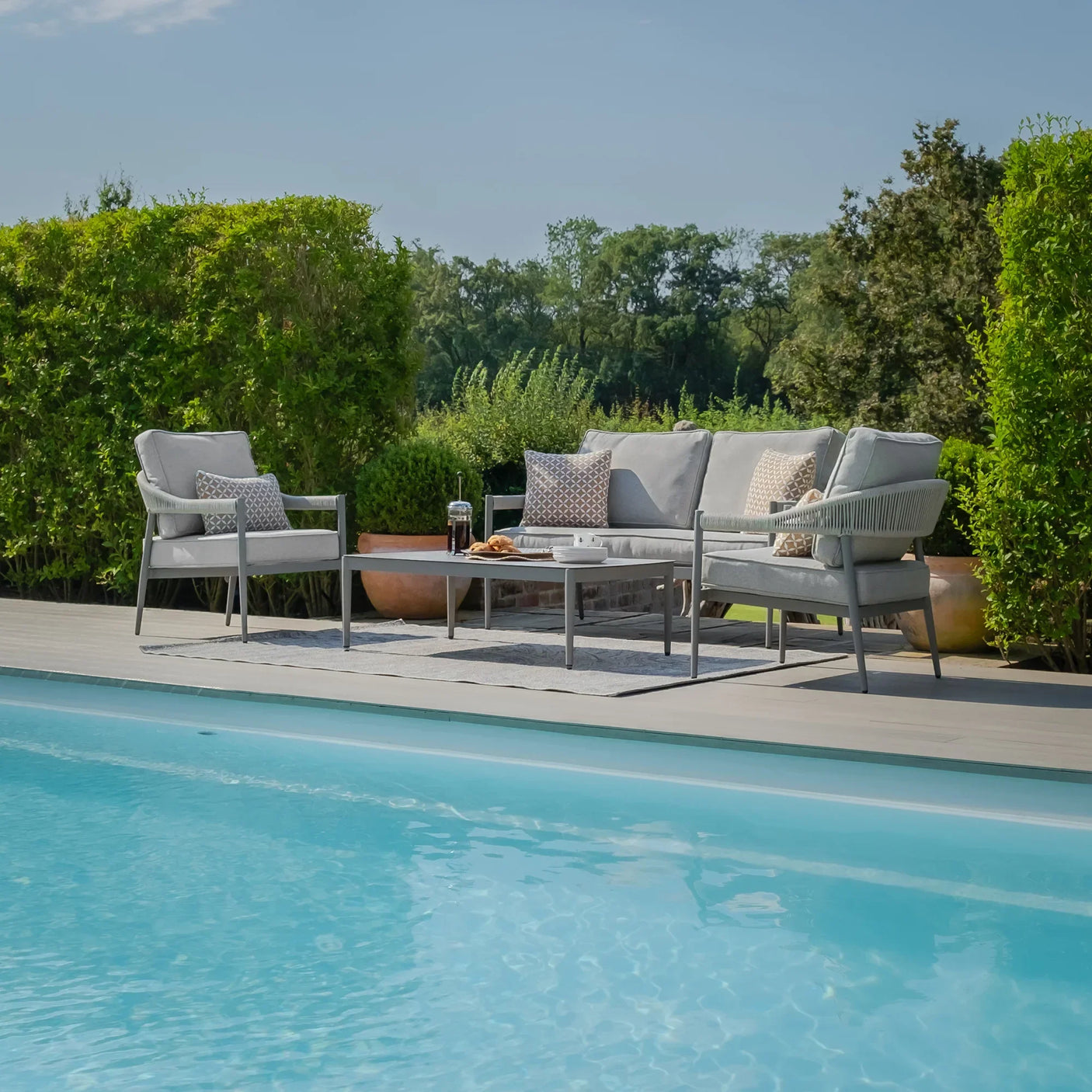 Grey outdoor sofa set with cushions and coffee table by a pool on a wooden patio