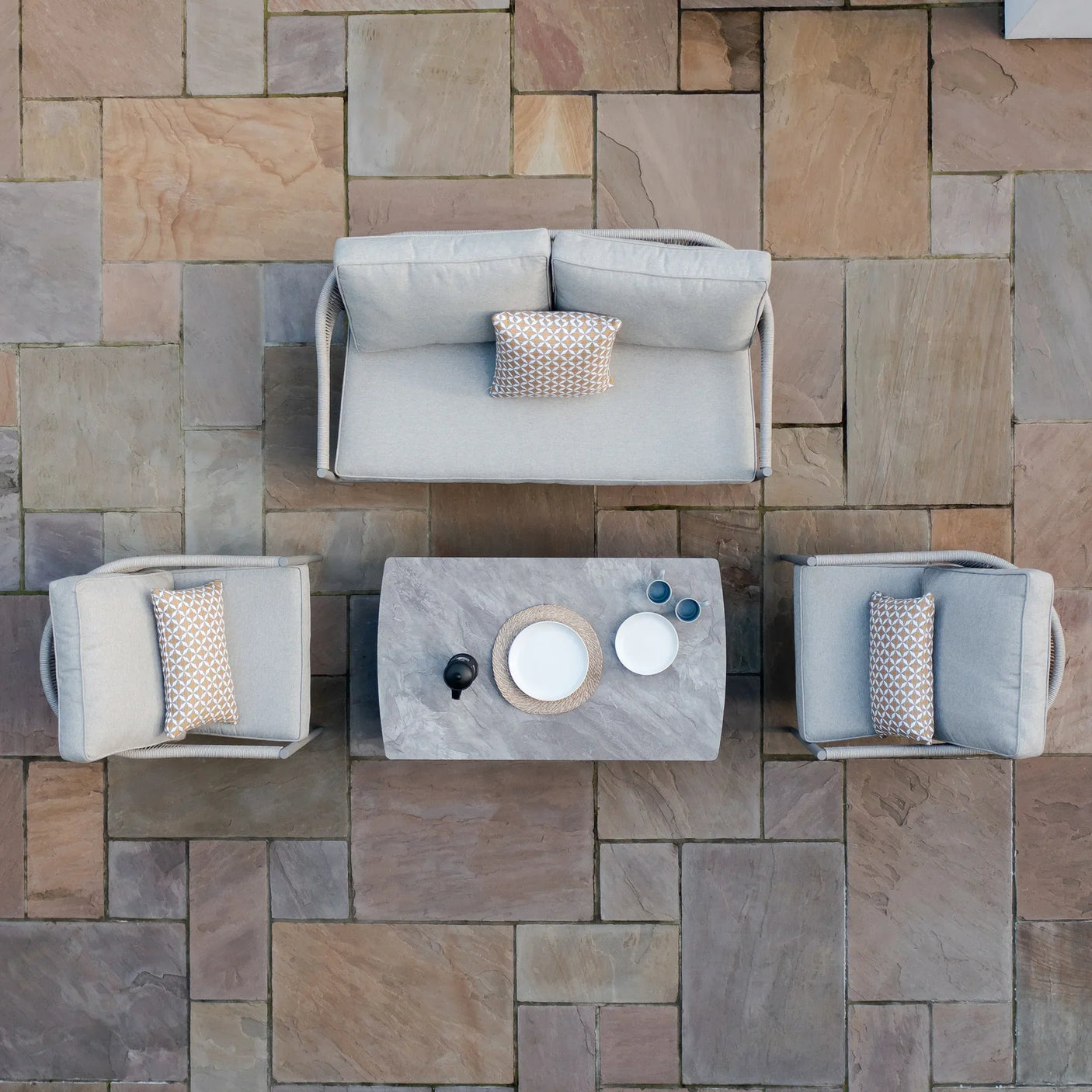 Grey outdoor sofa set with two armchairs and stone coffee table on patio tiles