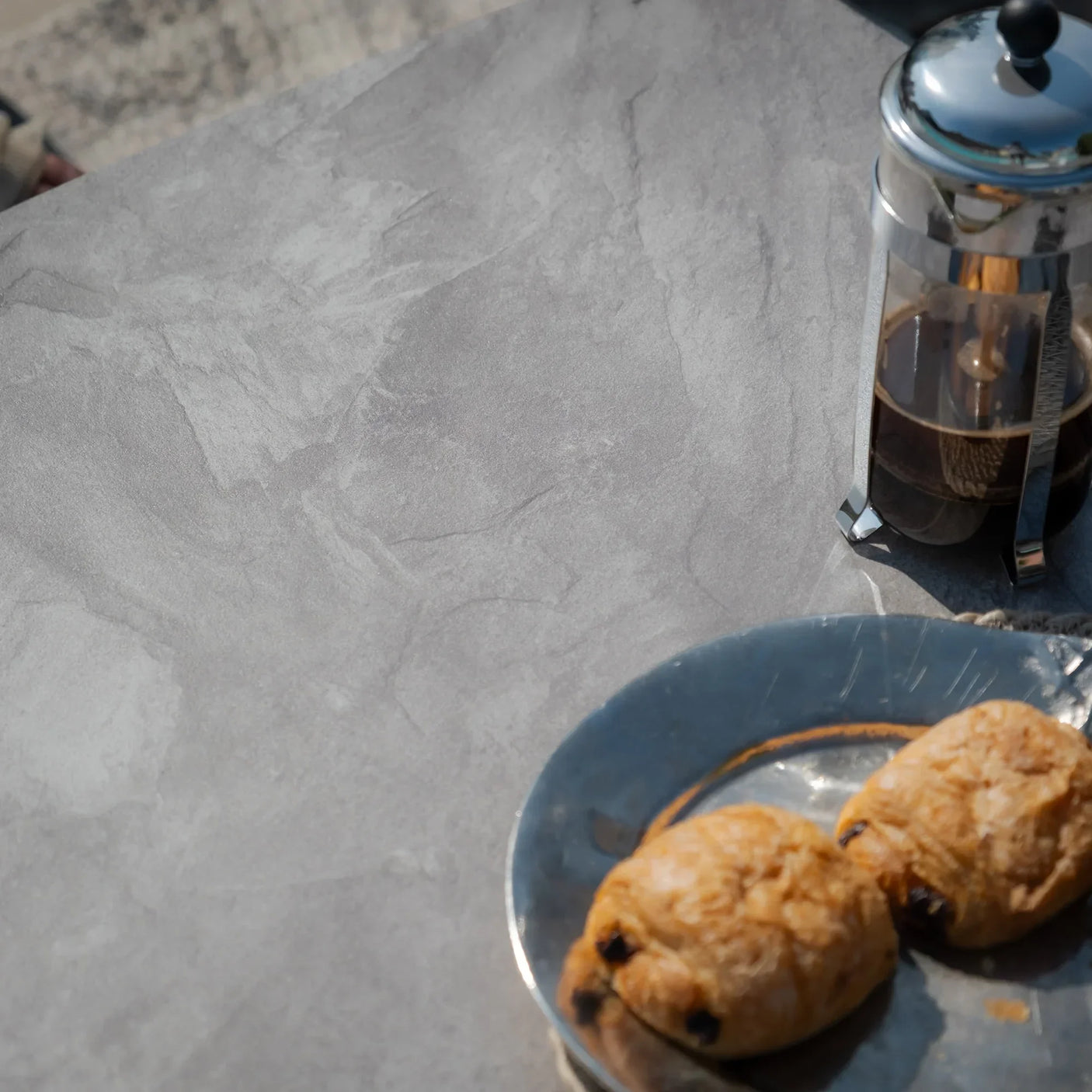 Grey stone effect dining table surface with French press and pastries on plate