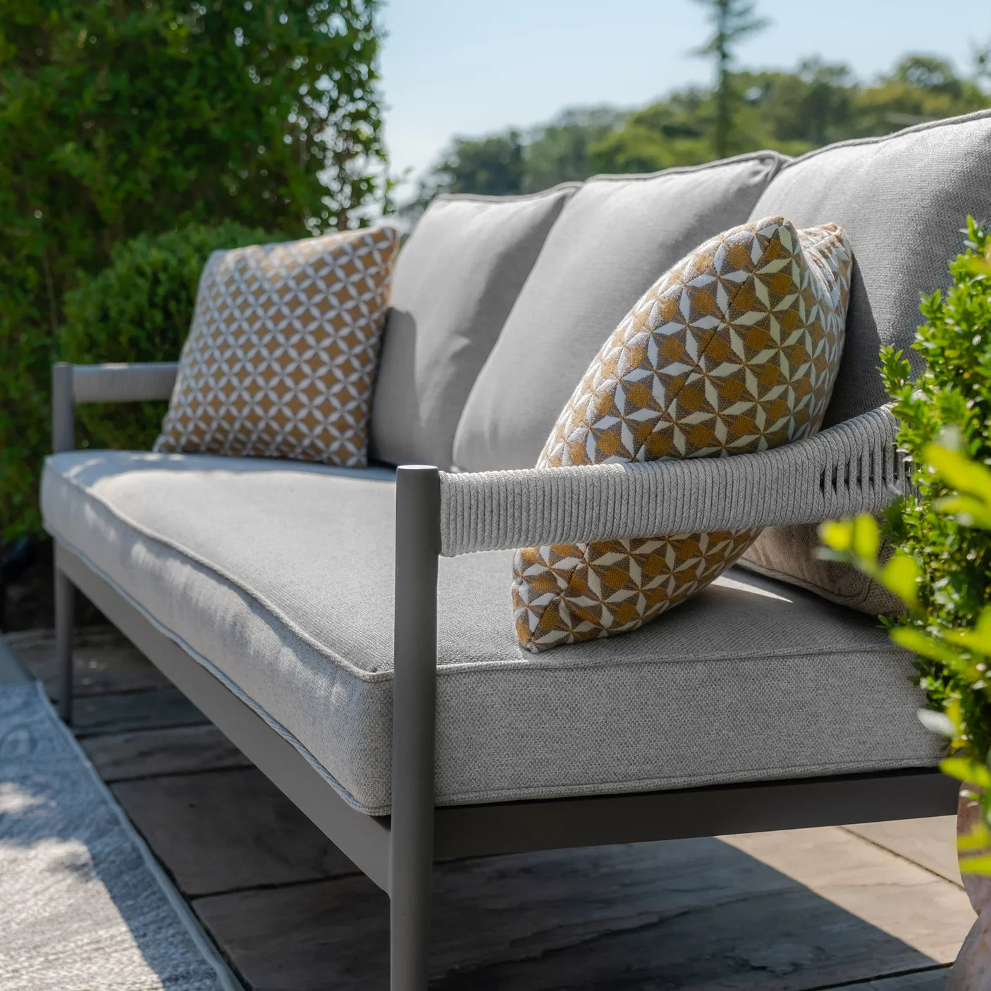 Grey outdoor sofa with rope armrests and patterned cushions on a patio