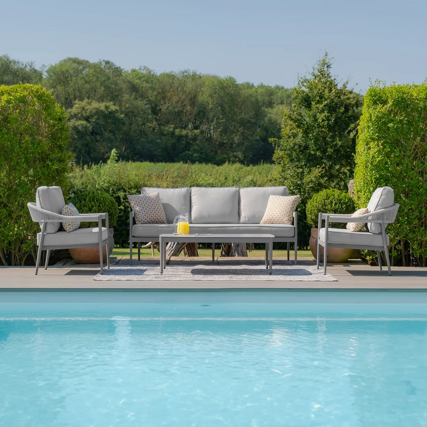 Grey outdoor sofa set with armchairs and table by pool on patio, garden view