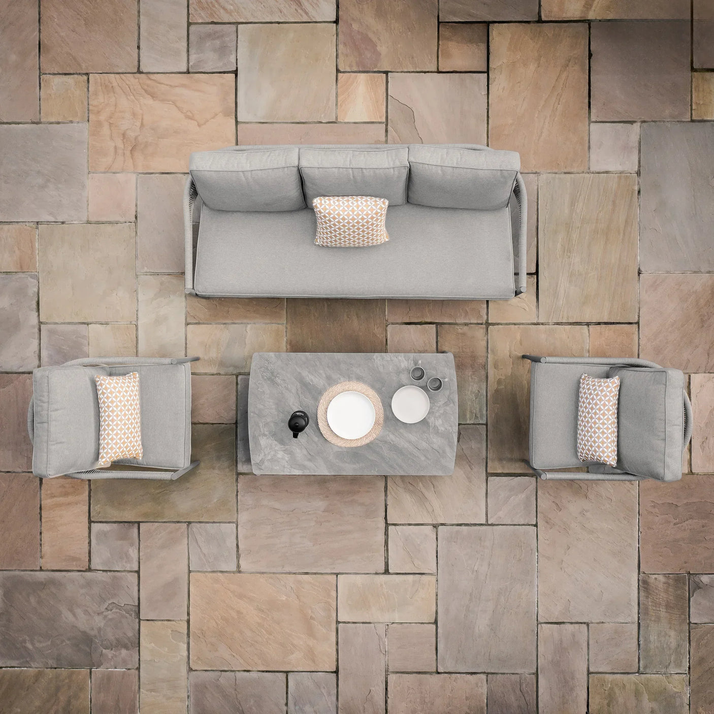 Grey outdoor sofa set with two armchairs and a stone coffee table on a paved patio