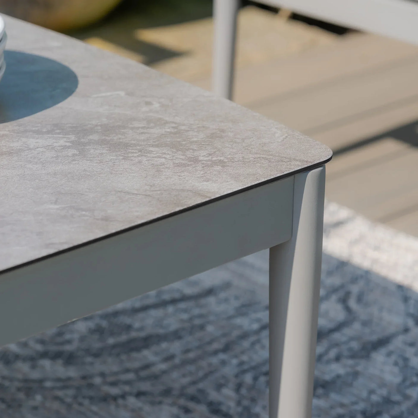 Rectangular outdoor dining table with grey stone-effect top and metal legs on deck
