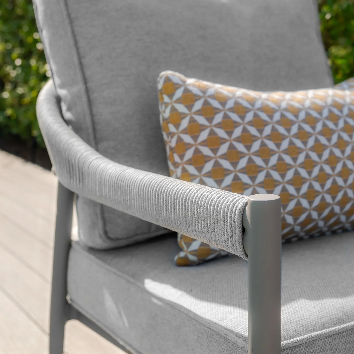 Grey outdoor garden chair with rope arm detail and patterned cushion on wooden decking