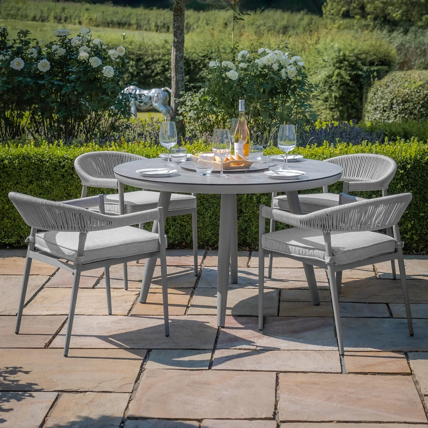 Grey outdoor dining set with round table and four rope chairs on stone patio