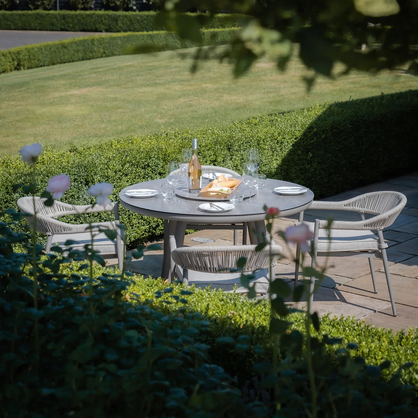 Grey outdoor dining set with round table and four rope chairs on garden patio