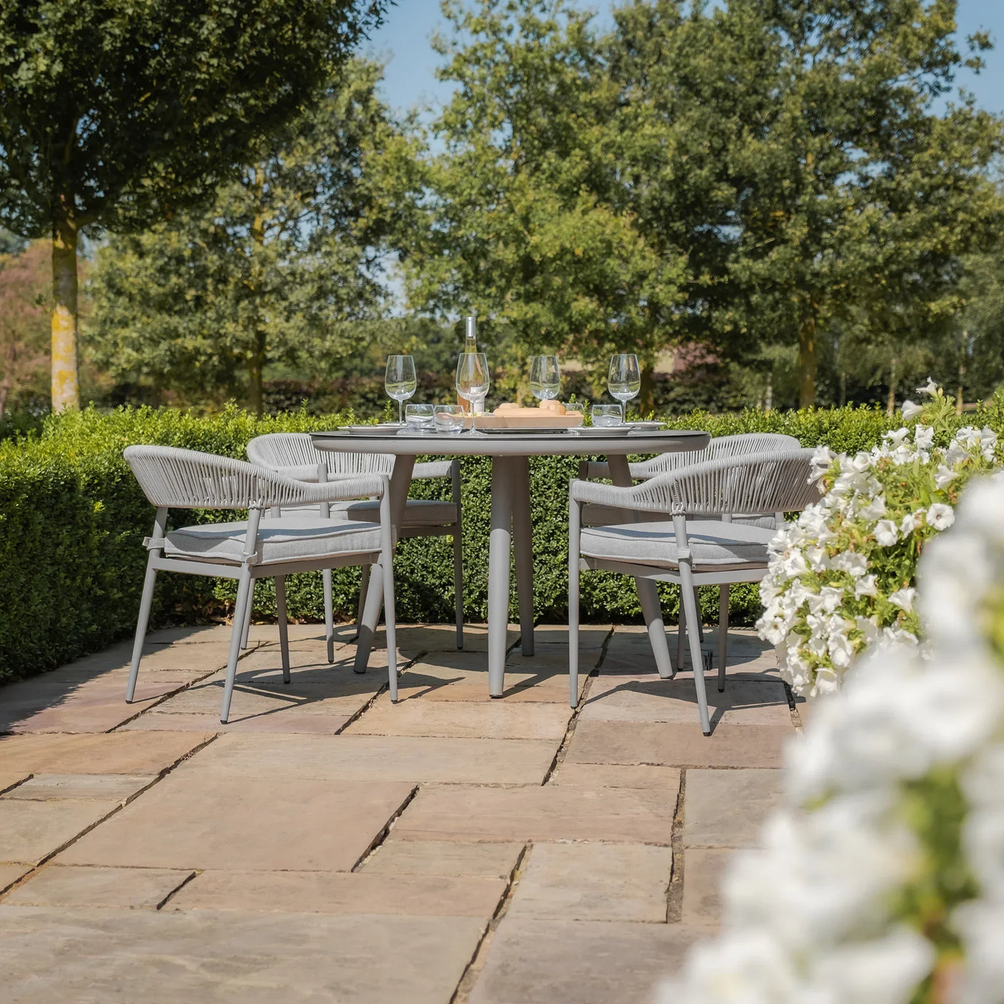 Grey outdoor dining set with four chairs and round table on stone patio in garden setting