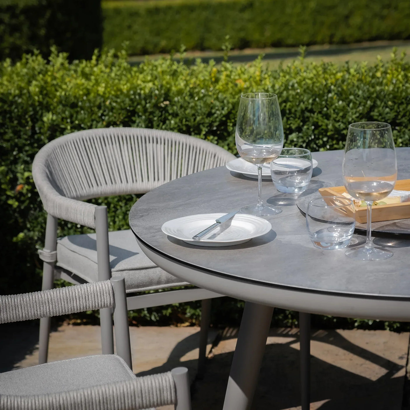 Grey outdoor dining table set with rope chairs, glassware, and plates on patio