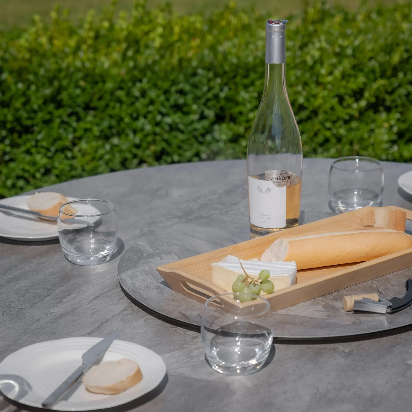 Round grey garden dining table set with wine, bread, cheese and glasses outdoors