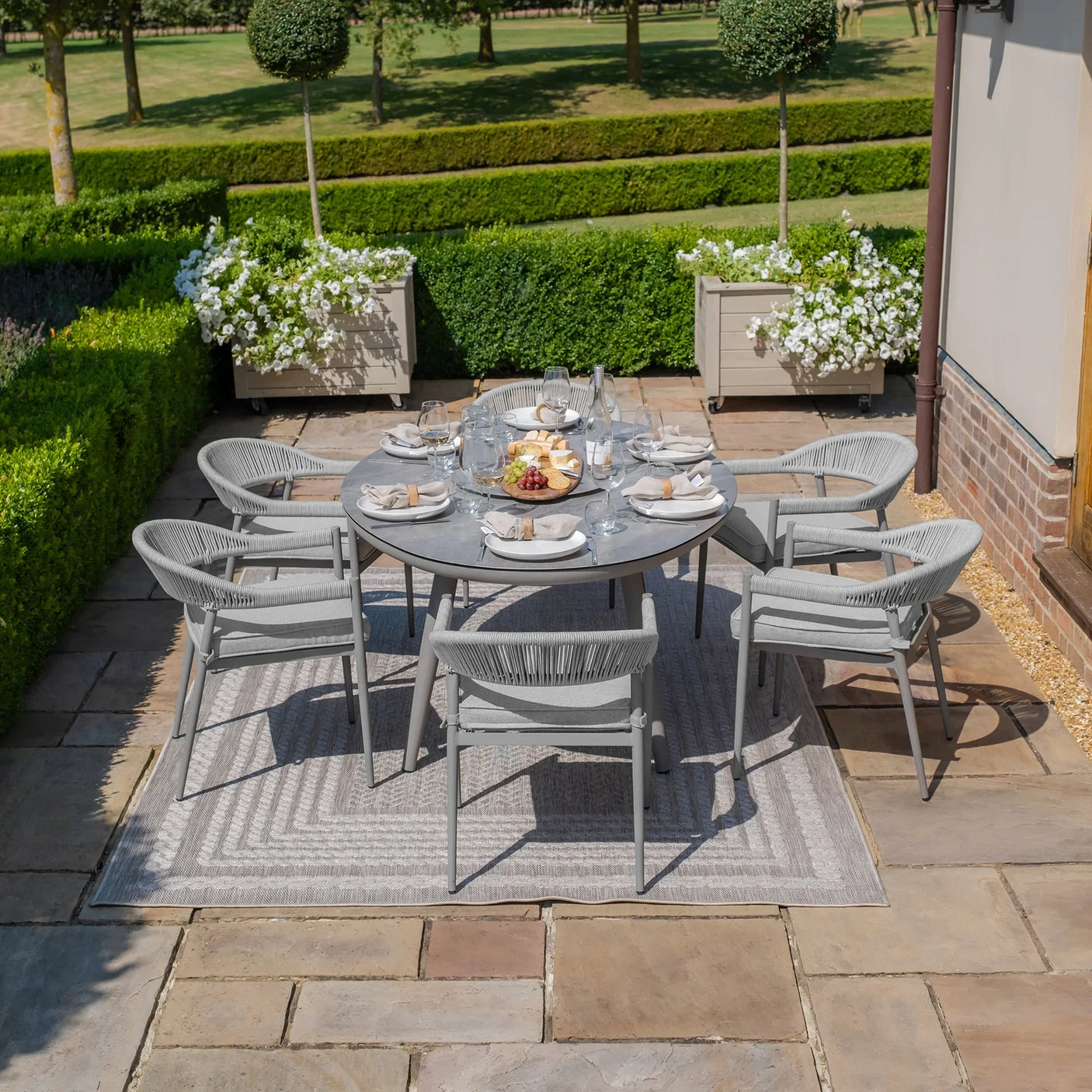 Grey outdoor dining set with six chairs on patio, round table set with plates and glasses