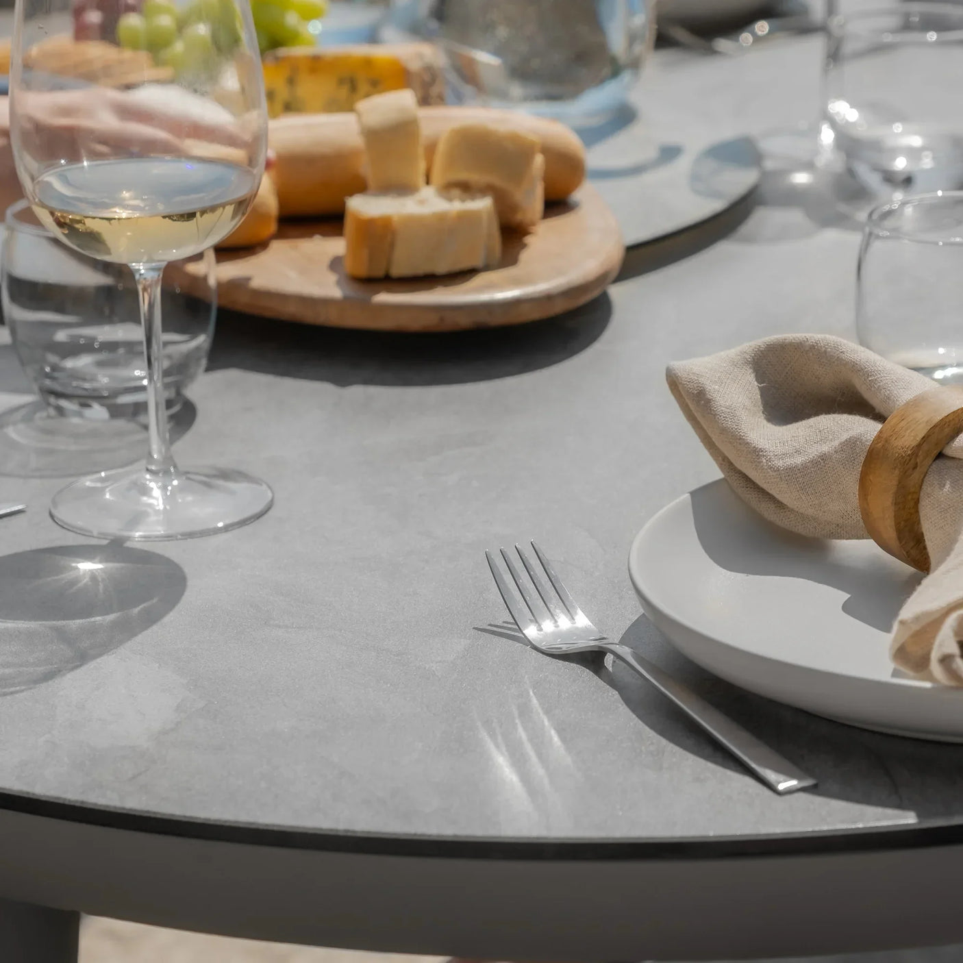 Grey dining table with bread, wine glass, plate, fork, and linen napkin on outdoor setting