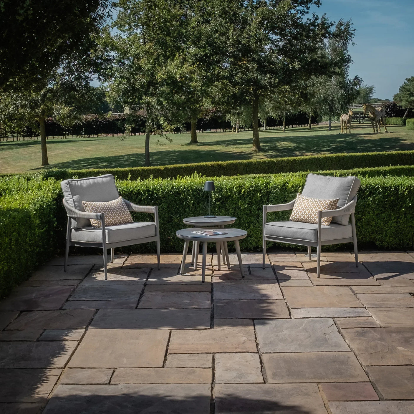 Grey outdoor lounge chair set with cushions and nesting tables on a stone patio