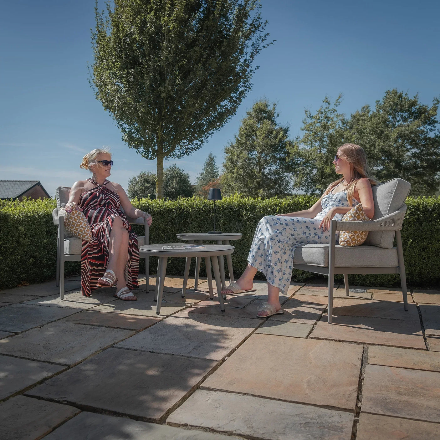 Grey outdoor lounge set with round coffee tables on patio, two women seated in armchairs