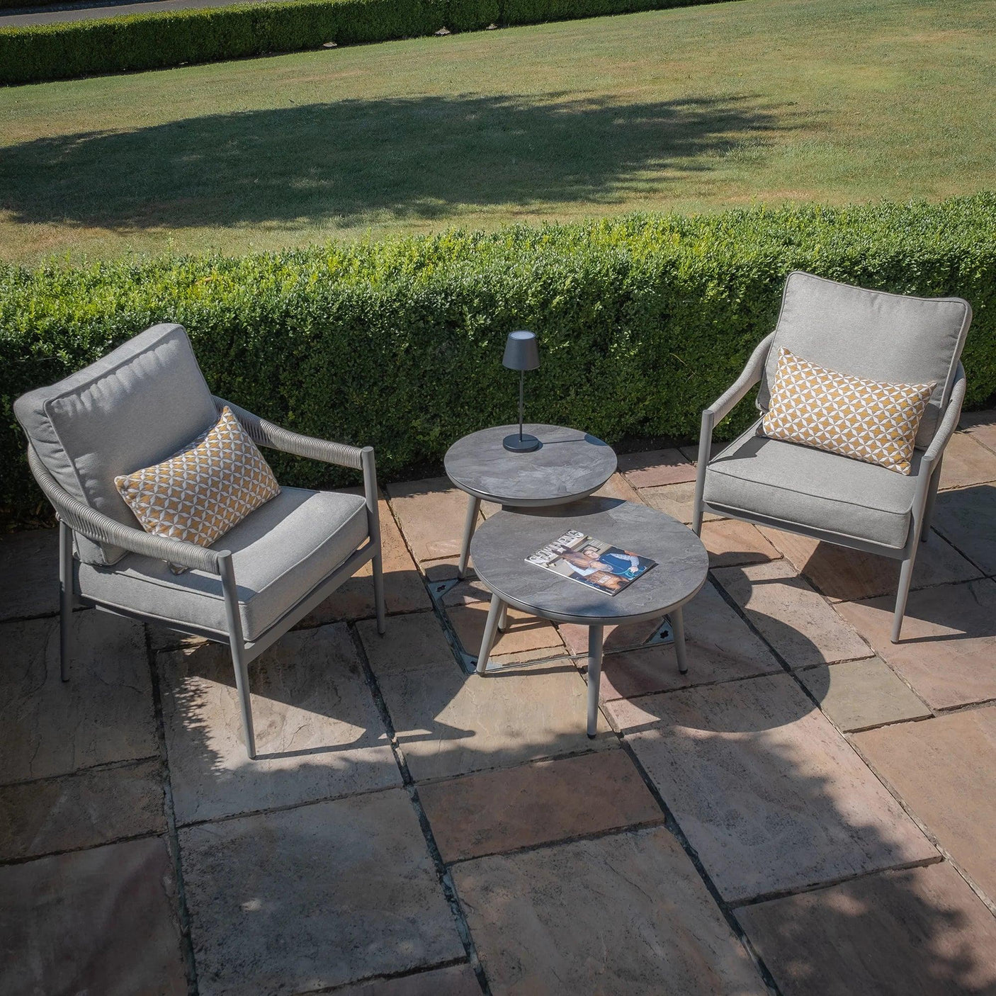 Grey outdoor lounge set with two armchairs, stone tables, and cushions on patio