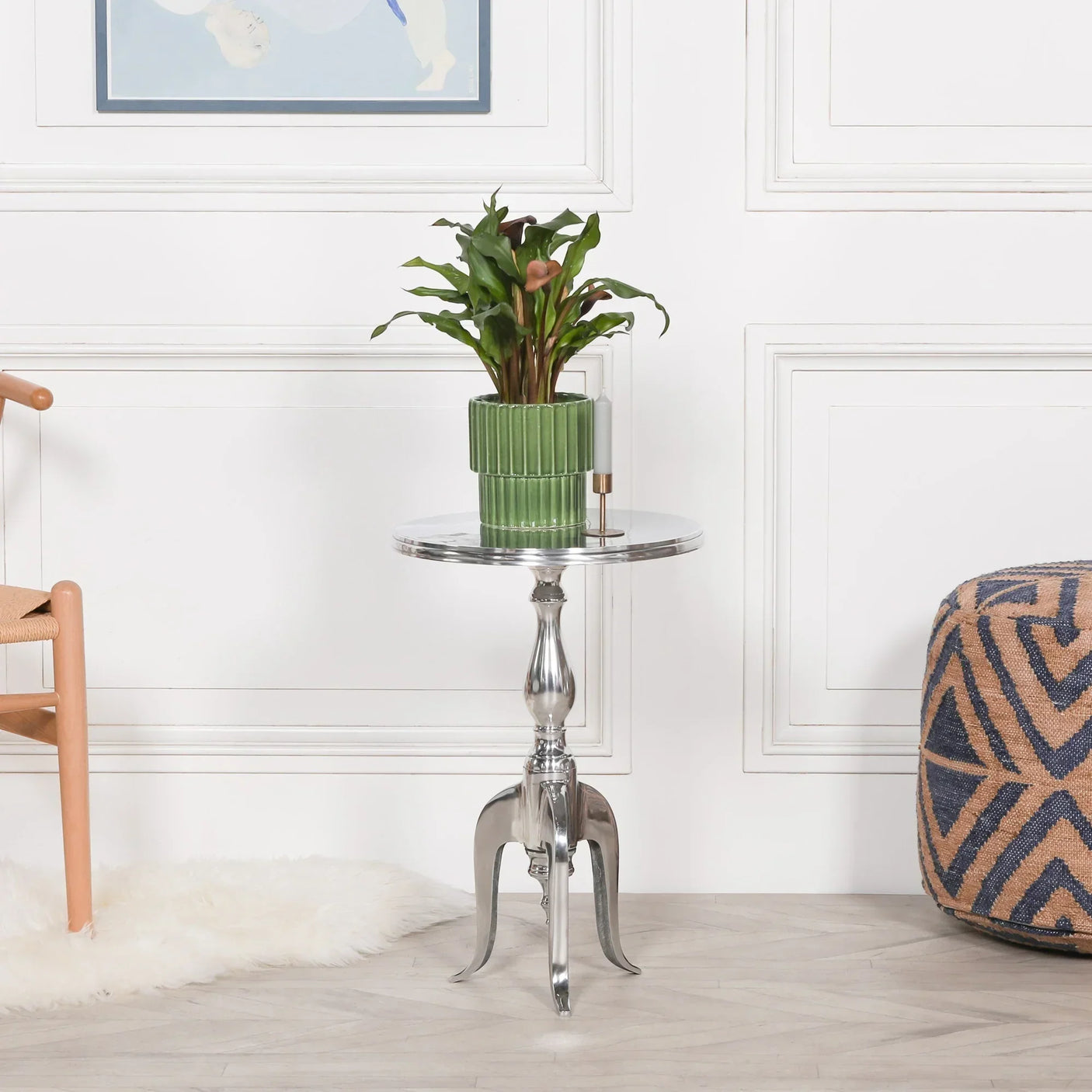Chrome round side table with ornate legs and green plant in ribbed pot in modern living room