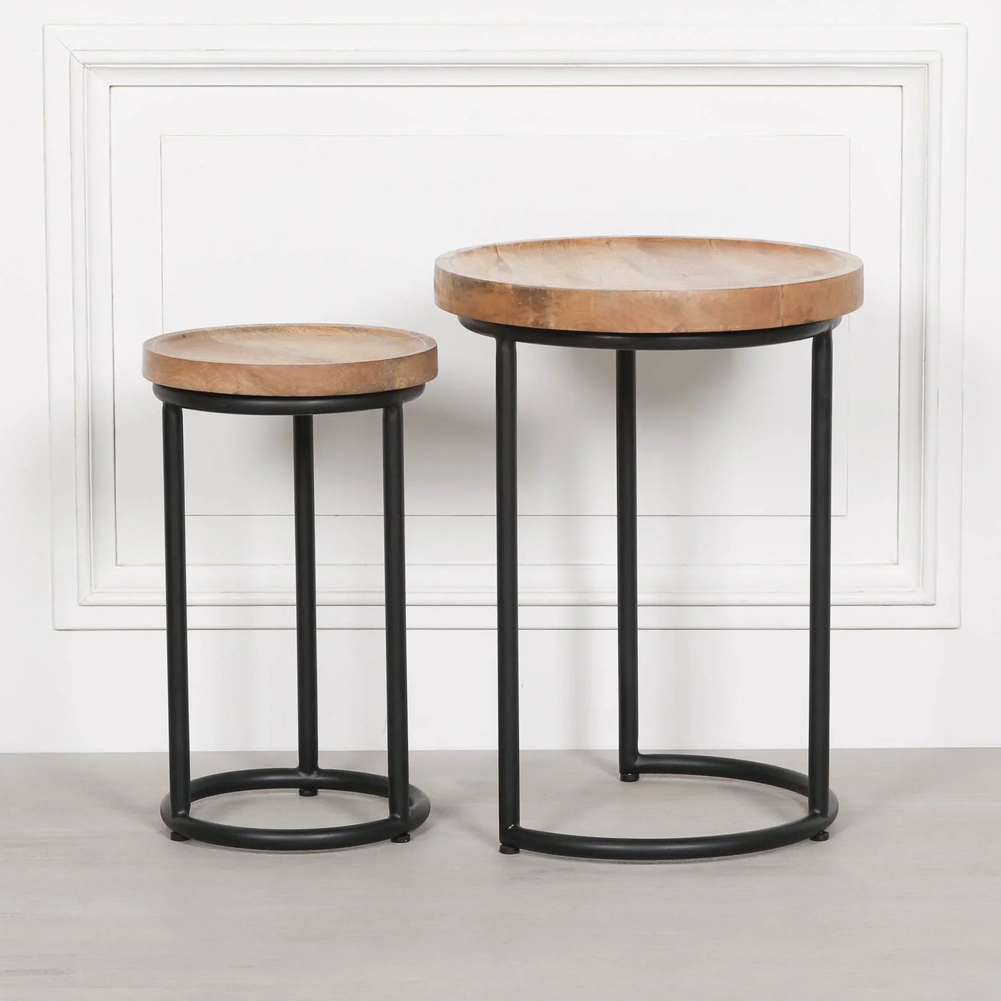 Round nested side tables with natural wood tops and black metal frames against white wall