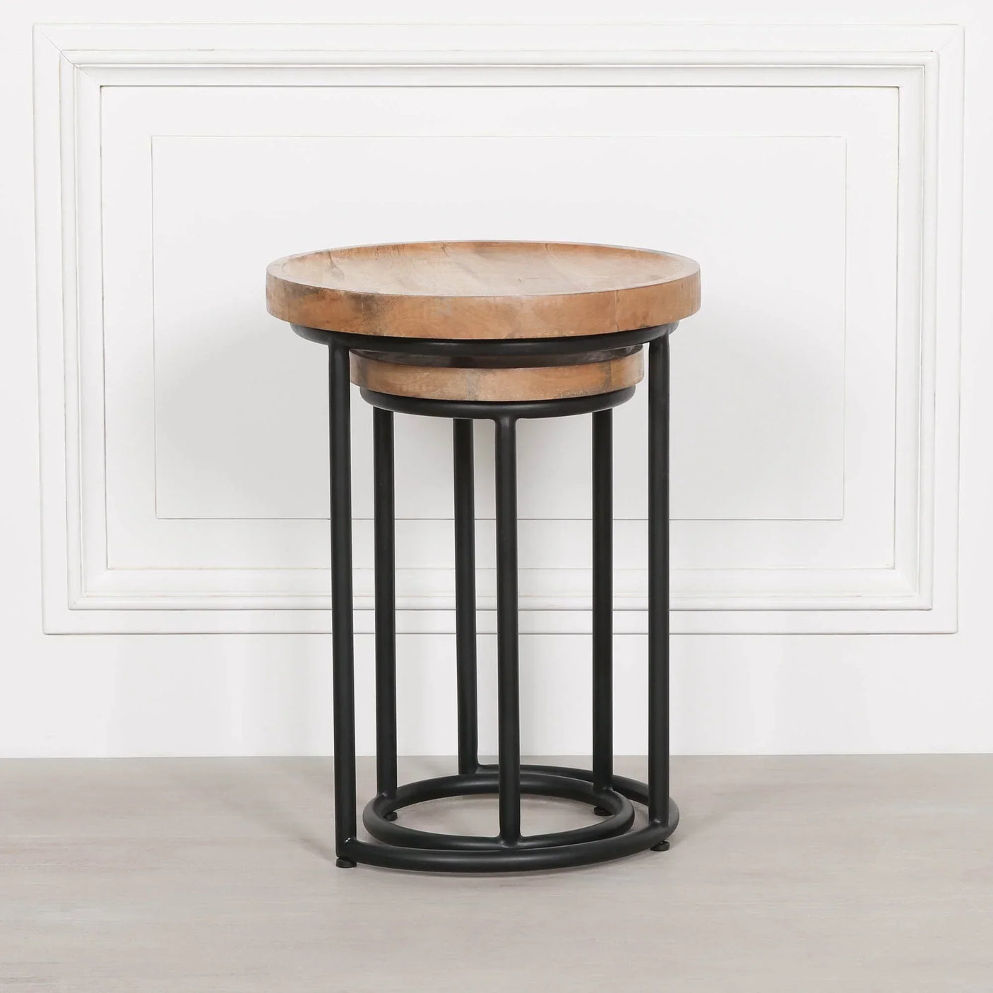 Round nesting tables with black metal legs and wooden tops against white panel wall
