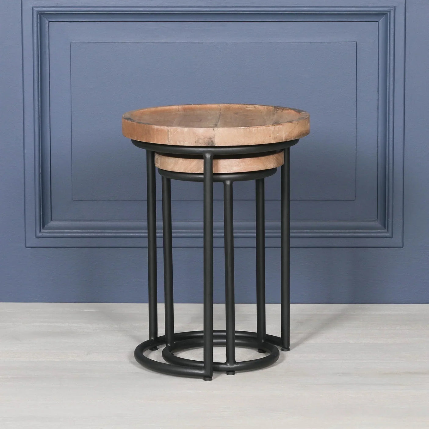 Round wooden side table with black metal frame against blue wall and light wood floor