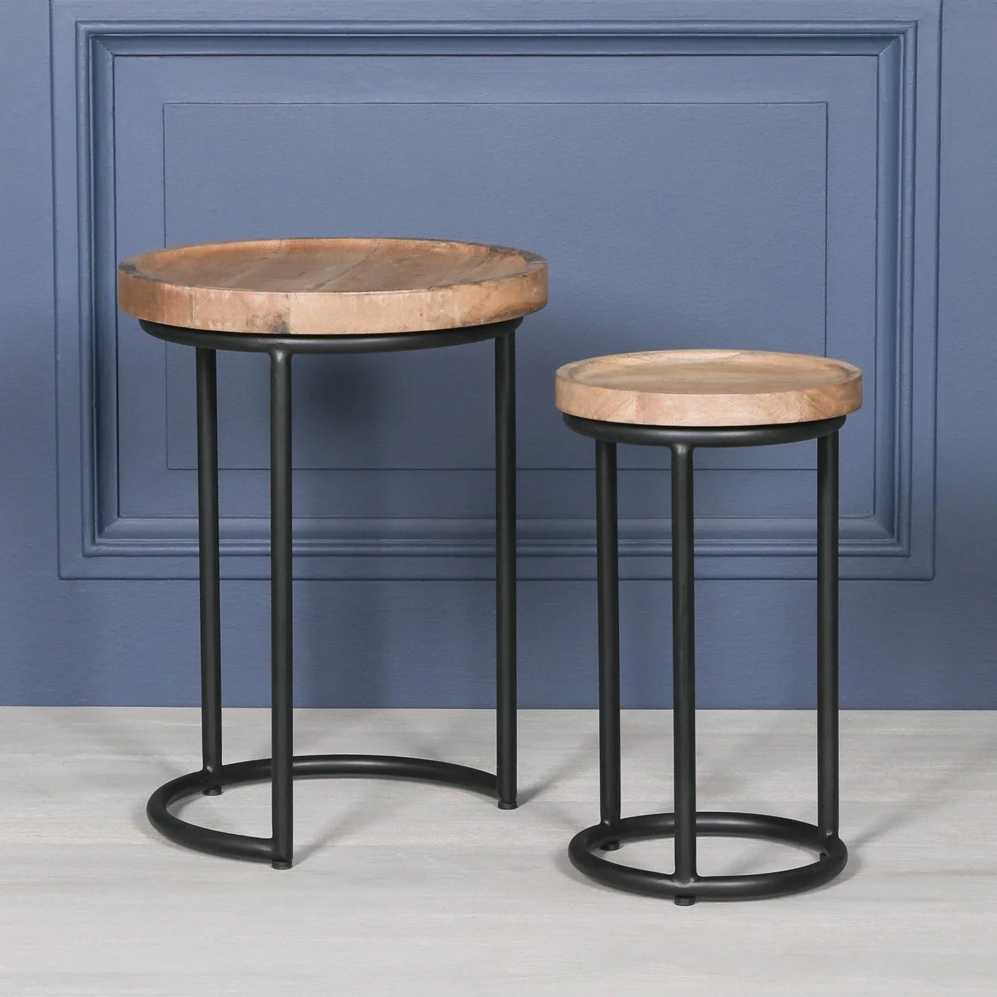 Set of two round wooden side tables with black metal frames on light floor